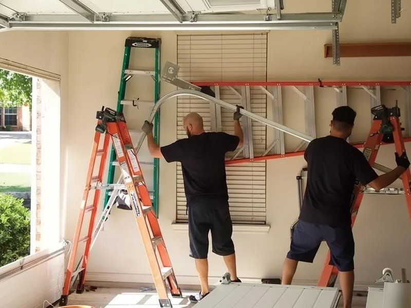 Two technicians on ladders working on a garage door