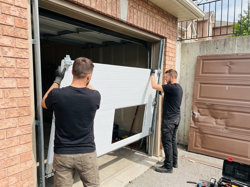 Two technicians carrying a replacement garage door panel