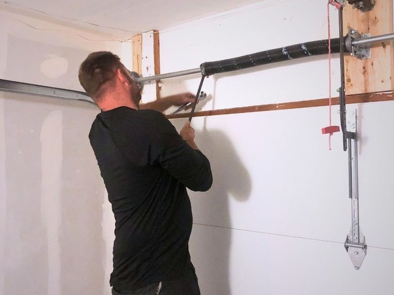 Technician winding a new torsion spring with winding bars above a garage door