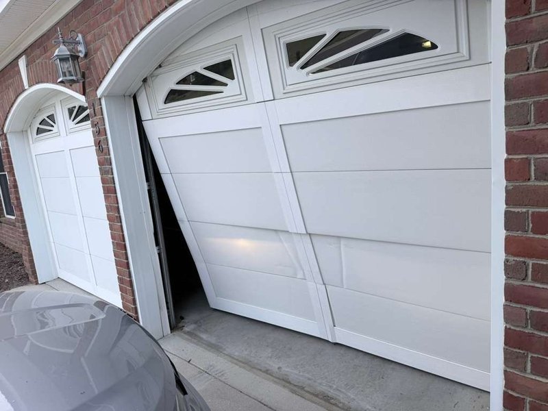 Off-track white garage door jammed at an angle at a brick home